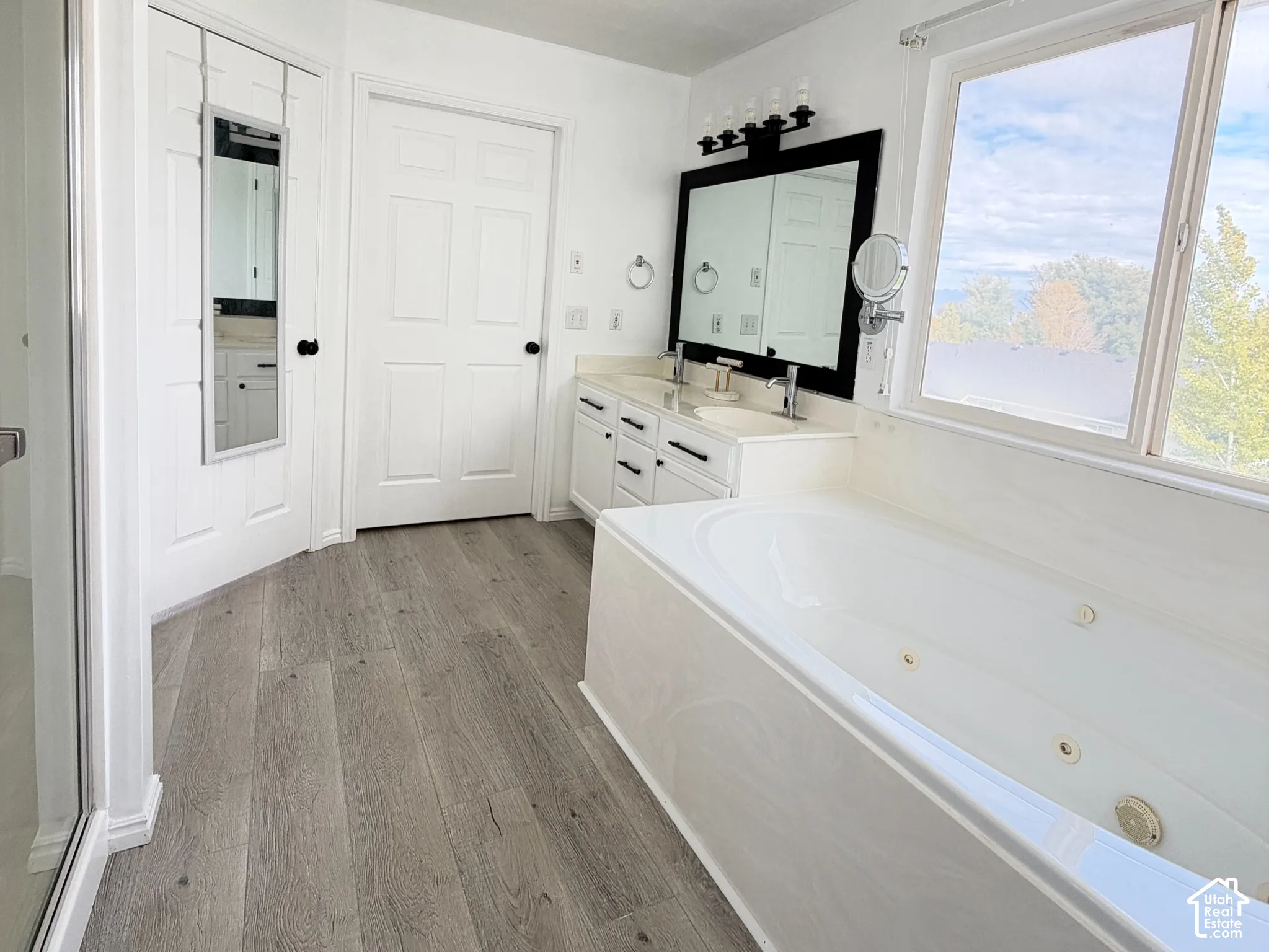 Master Bathroom featuring wood-finish flooring, a built-in jetted tub, a dual-sink vanity with a dark-framed mirror, and recessed ceiling lighting