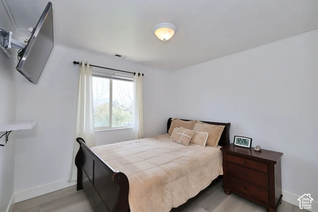 Bedroom interior featuring wood-finish flooring, a wall-mounted television bracket, a sliding window with a curtain rod, and a flush-mount ceiling light