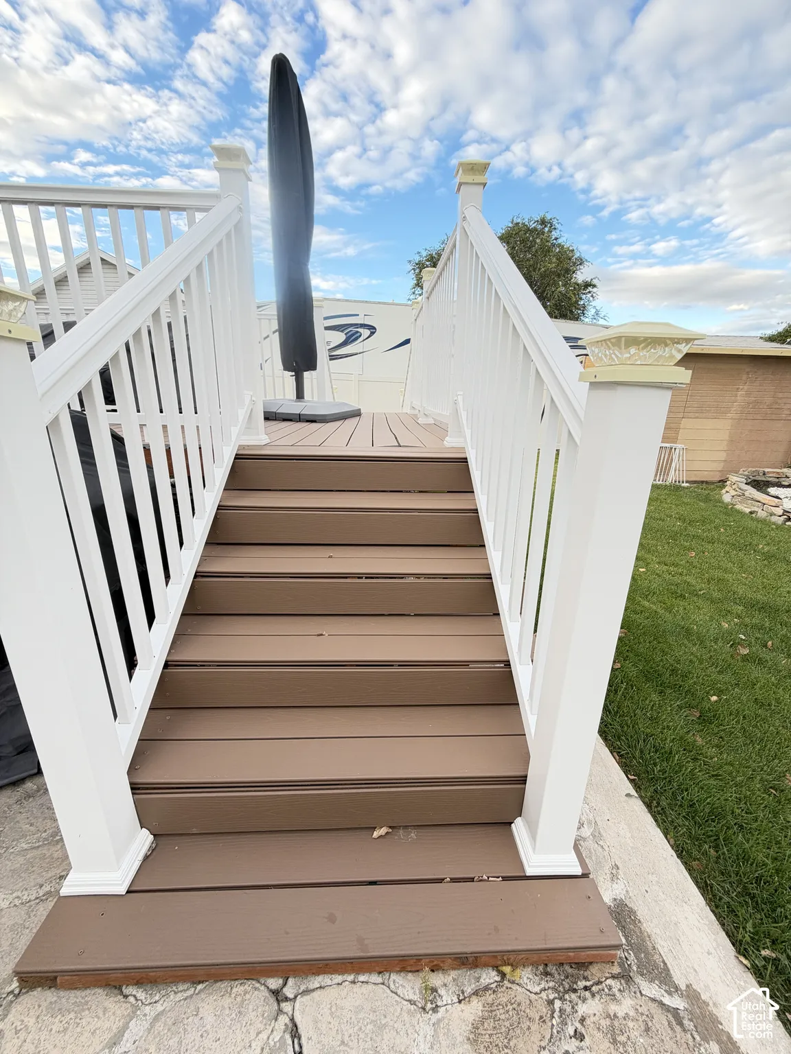 Elevated deck featuring composite decking, white vinyl railings, post-cap lighting, and concrete hardscaping