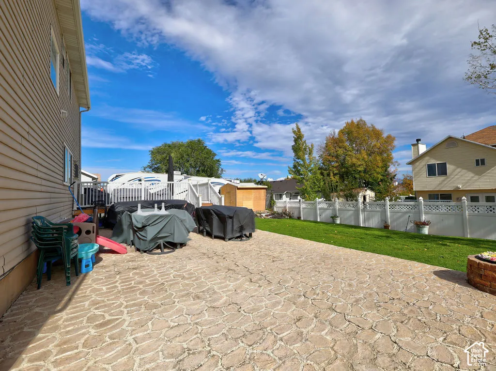 Rear yard featuring a stamped concrete patio, manicured lawn, white vinyl fencing, and a stone-style fire pit