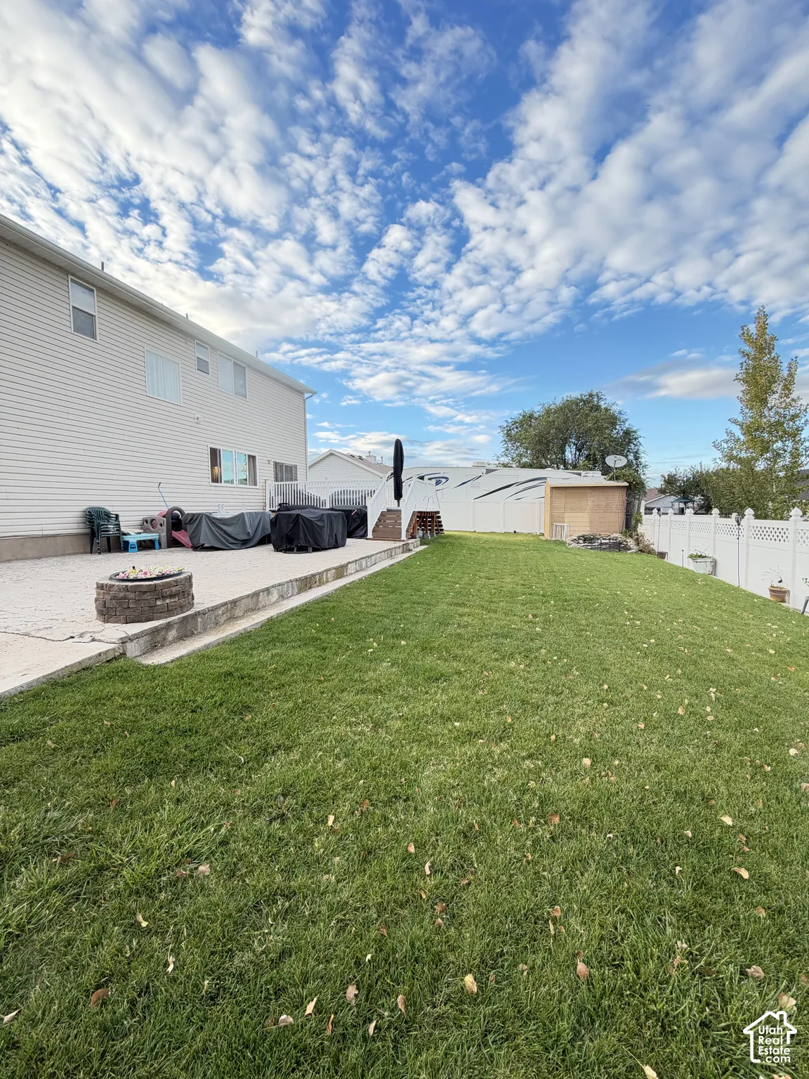 Expansive backyard featuring a leveled lawn, concrete patio, stone-veneer fire pit, and full-height vinyl privacy fencing