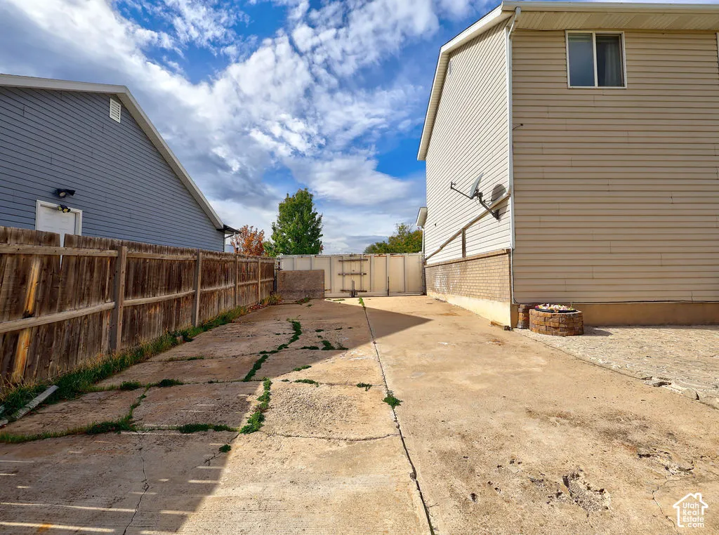 Concrete side yard featuring wood fencing, masonry perimeter wall, and a stone-built fire pit