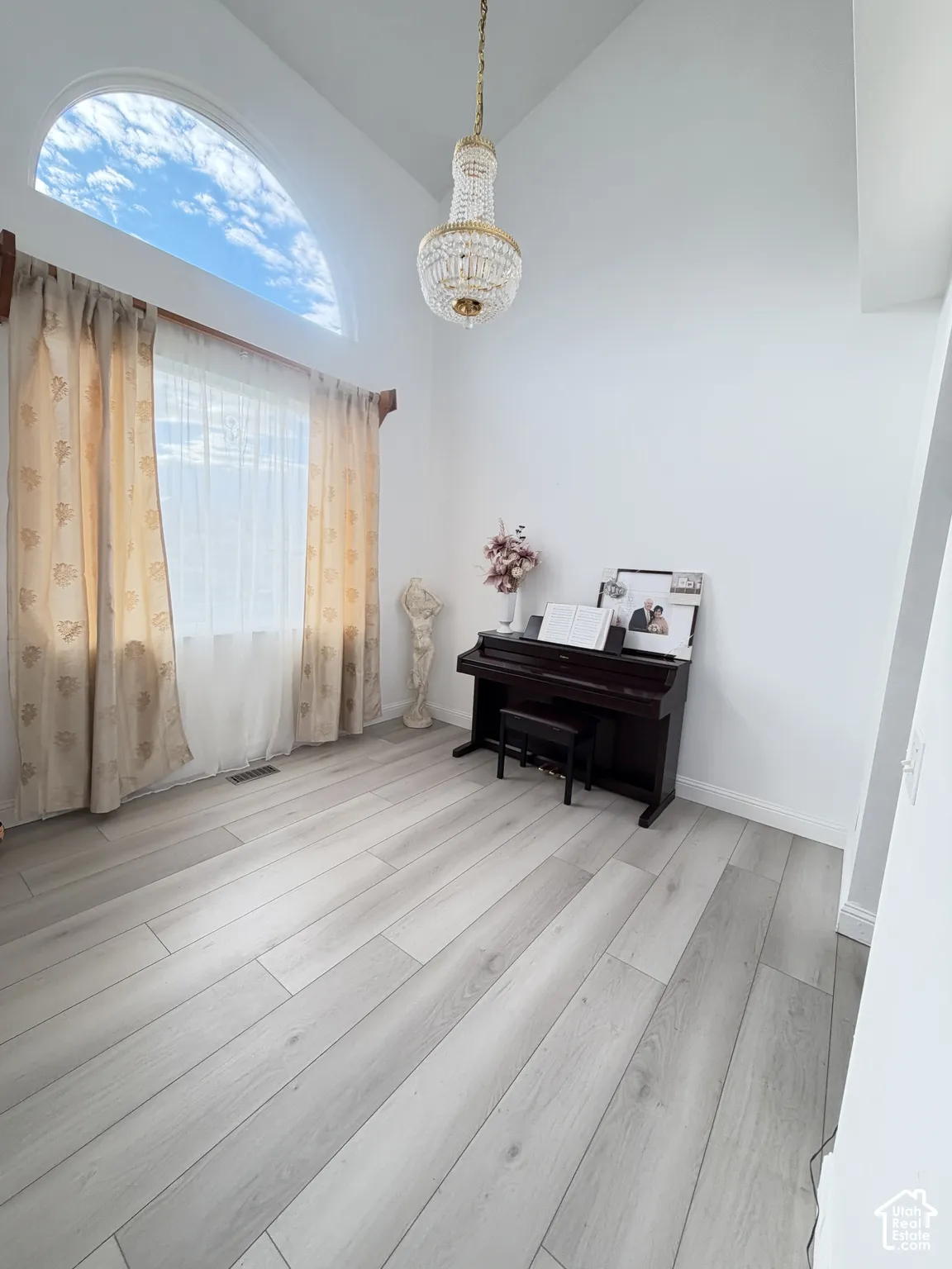 Vaulted ceilings featuring an arched window, wood-finish flooring, and a crystal chandelier