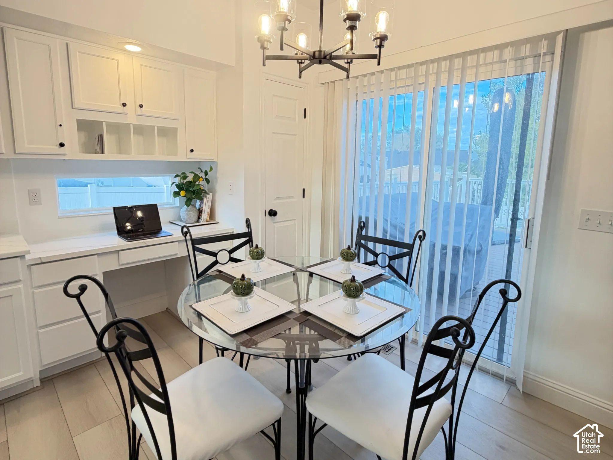 Dining area featuring wood-finish flooring, white cabinetry with built-in desk space, a multi-arm chandelier, and sliding glass doors