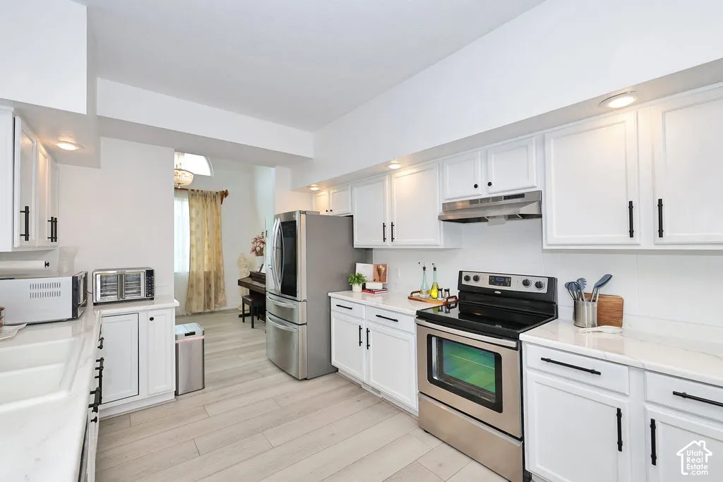 Kitchen featuring white cabinetry with matte black hardware, stone-finish countertops, stainless steel appliances, and wood-finish flooring