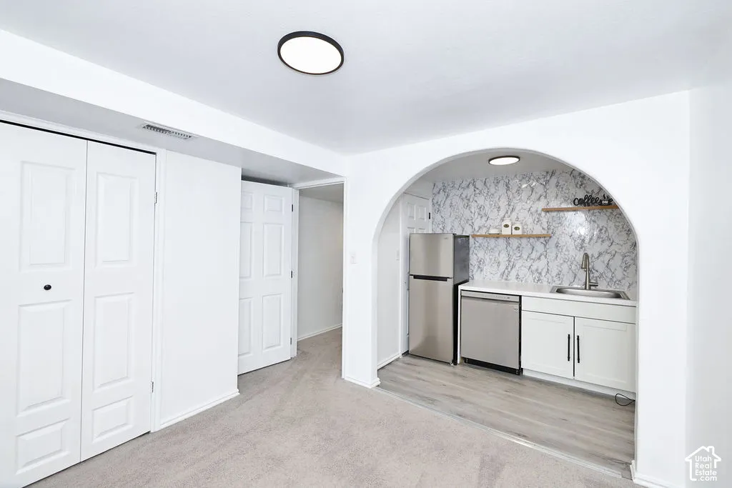 Archway entryway featuring wood-finish flooring, custom stone-patterned backsplash, stainless steel appliances, white shaker cabinetry, and floating wall shelves