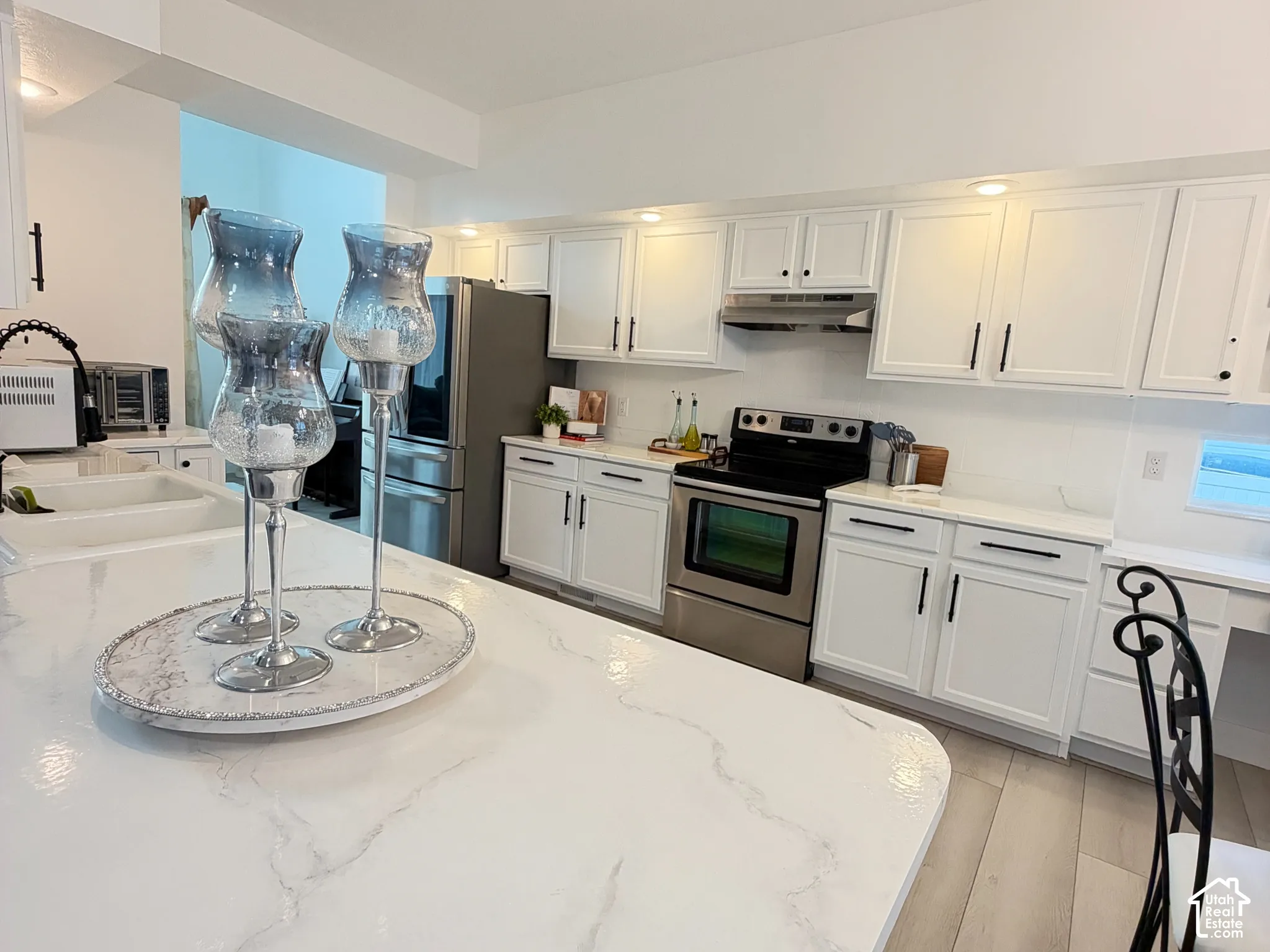 Kitchen featuring white shaker-style cabinetry, a stone-finish island countertop, stainless steel appliances, and wood-finish flooring
