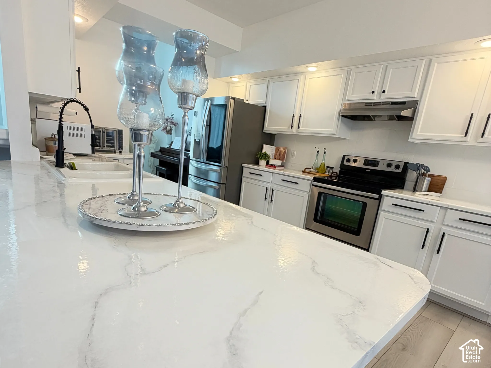 Kitchen featuring white cabinetry with matte black hardware, stone-patterned countertops, wood-finish flooring, and a stainless steel range and refrigerator