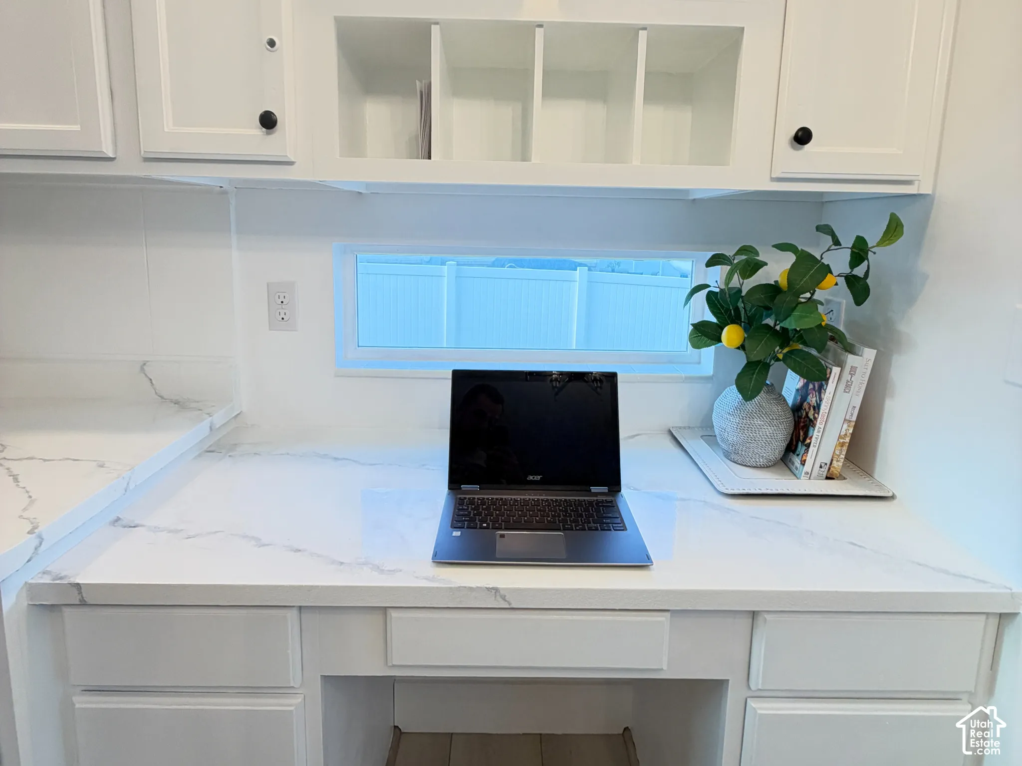 Built-in desk area featuring stone-surface countertop, white shaker-style cabinetry, open shelving, and horizontal transom window