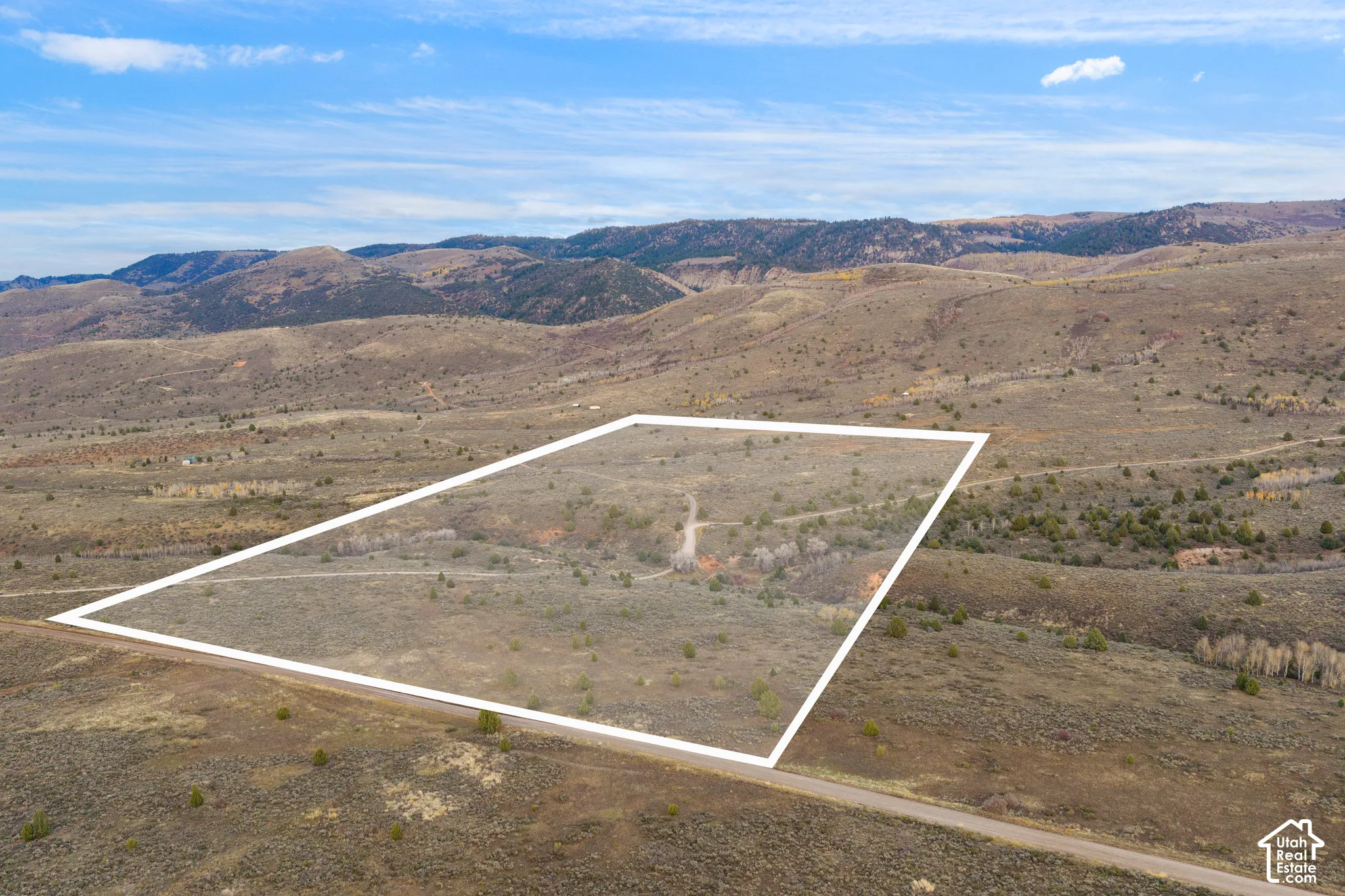 Expansive plot of land featuring natural vegetation, gently rolling topography, mountain backdrops, and direct road frontage