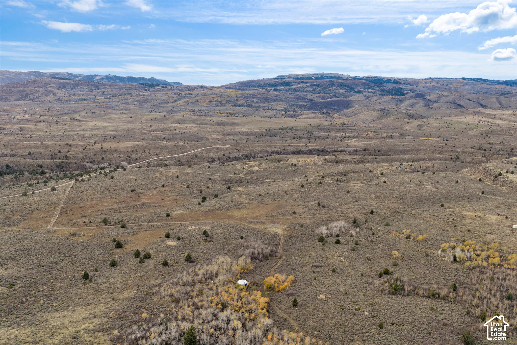 Expansive terrain featuring native high-desert vegetation, scattered mature trees, and mountainous topography