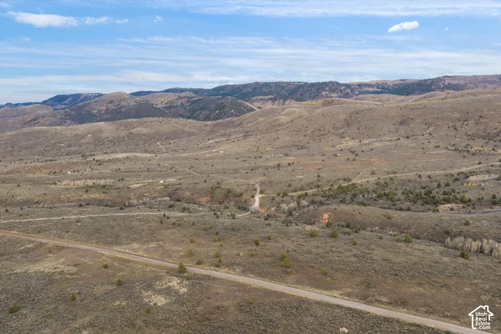 Expansive landscape featuring rolling topography, native vegetation, earthen terrain, and mountain silhouettes