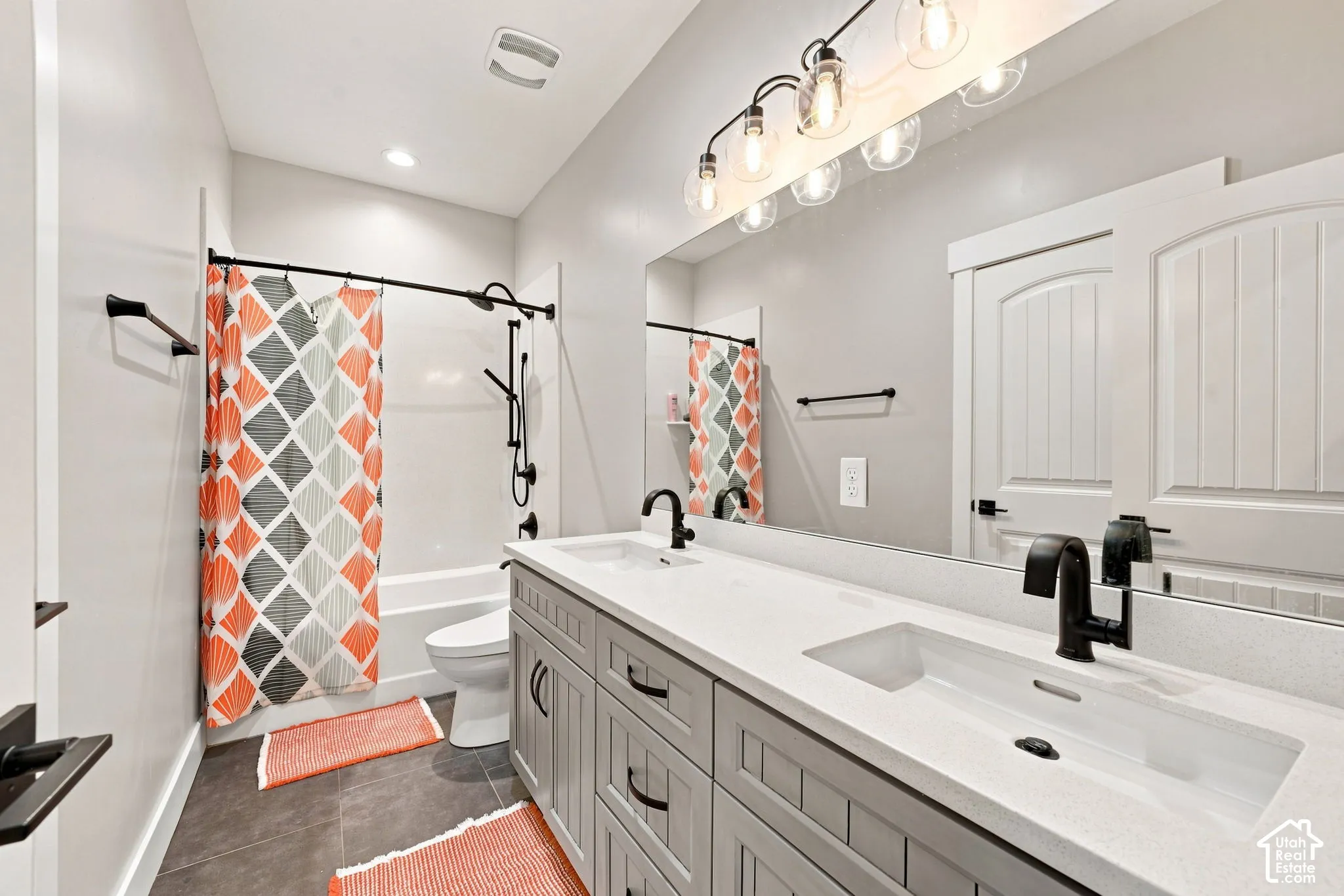 Dual-sink vanity with light-toned countertop, custom gray cabinetry, matte black hardware, and an expansive wall-mounted mirror