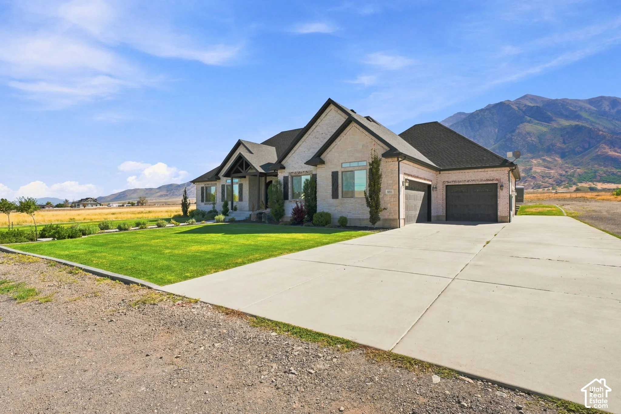 Single-story brick exterior featuring a multi-gabled roofline, three-car garage, expansive concrete driveway, manicured lawn, and mountain backdrop