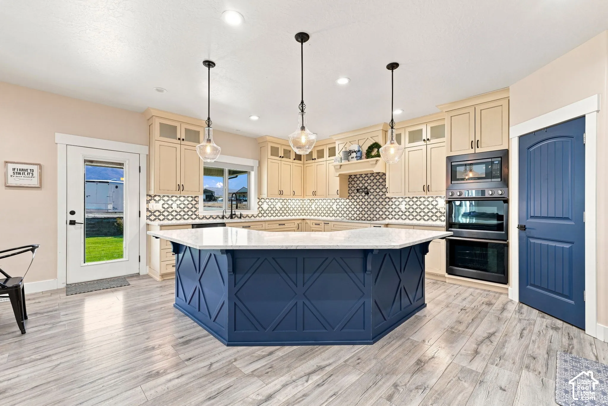 Kitchen featuring a blue-accented center island with a stone-style countertop, custom cabinetry, stainless steel double wall ovens, geometric pattern tile backsplash, and wood-finish flooring