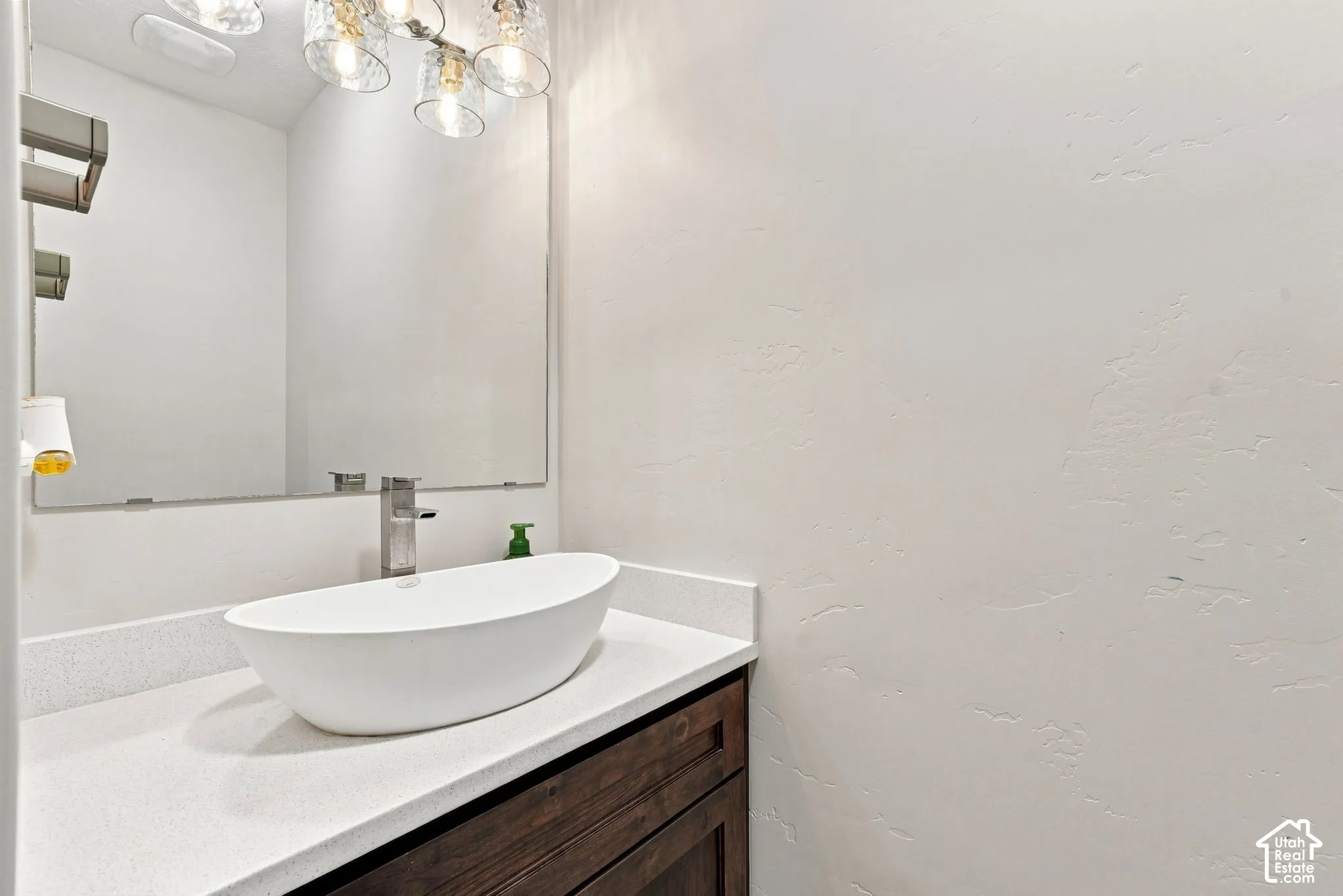 Wall-mounted vanity featuring a white vessel sink, quartz countertop, and dark wood-finish cabinetry, complemented by a large frameless mirror and glass-globe multi-light fixture