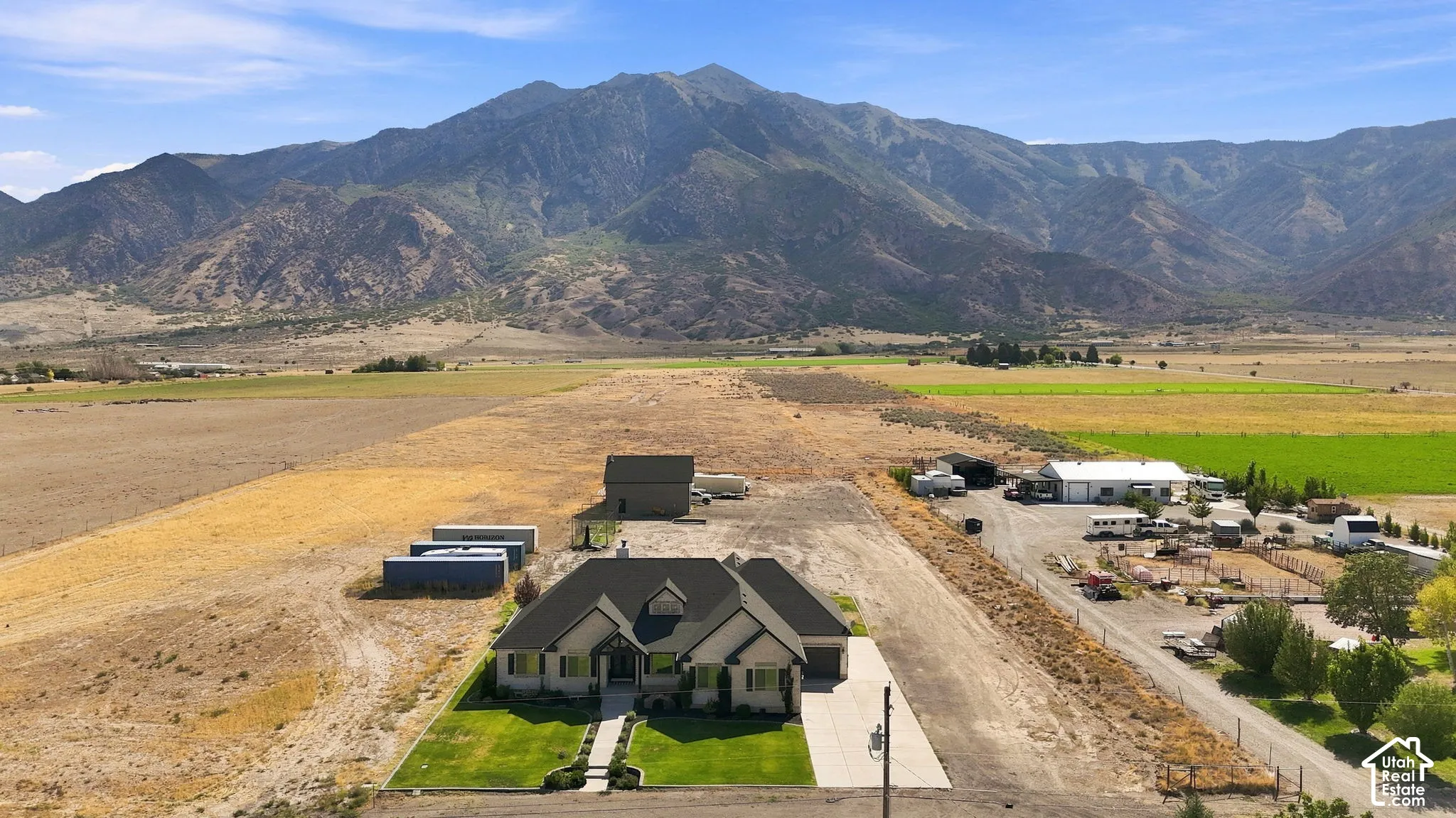 Single-story residence featuring a dark shingled roof, light-toned exterior siding, an attached garage, and prominent mountain backdrops on expansive acreage