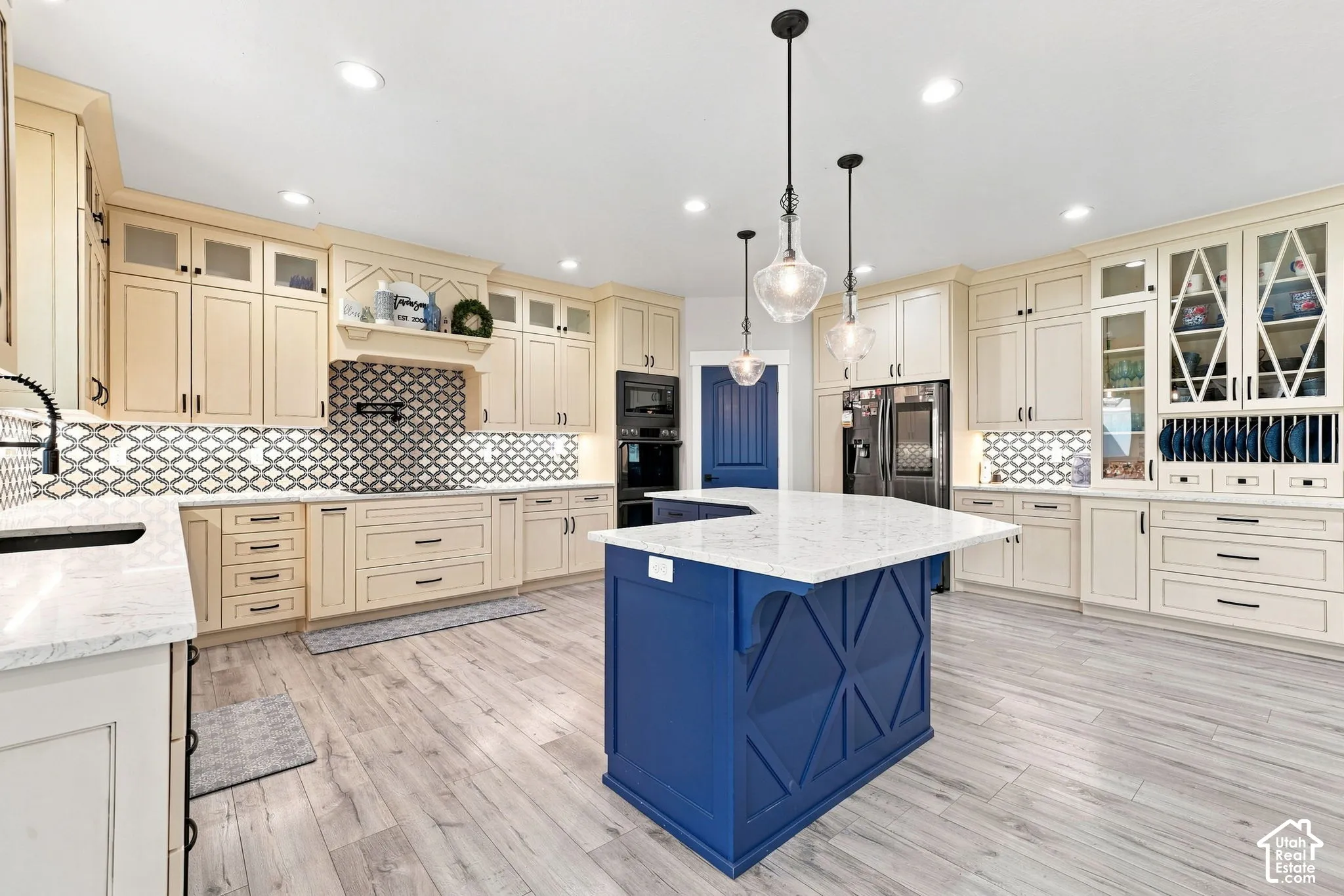 Kitchen featuring custom light-toned cabinetry with glass-front uppers, a central island with decorative woodwork, quartz countertops, patterned tile backsplash, and wood-finish flooring