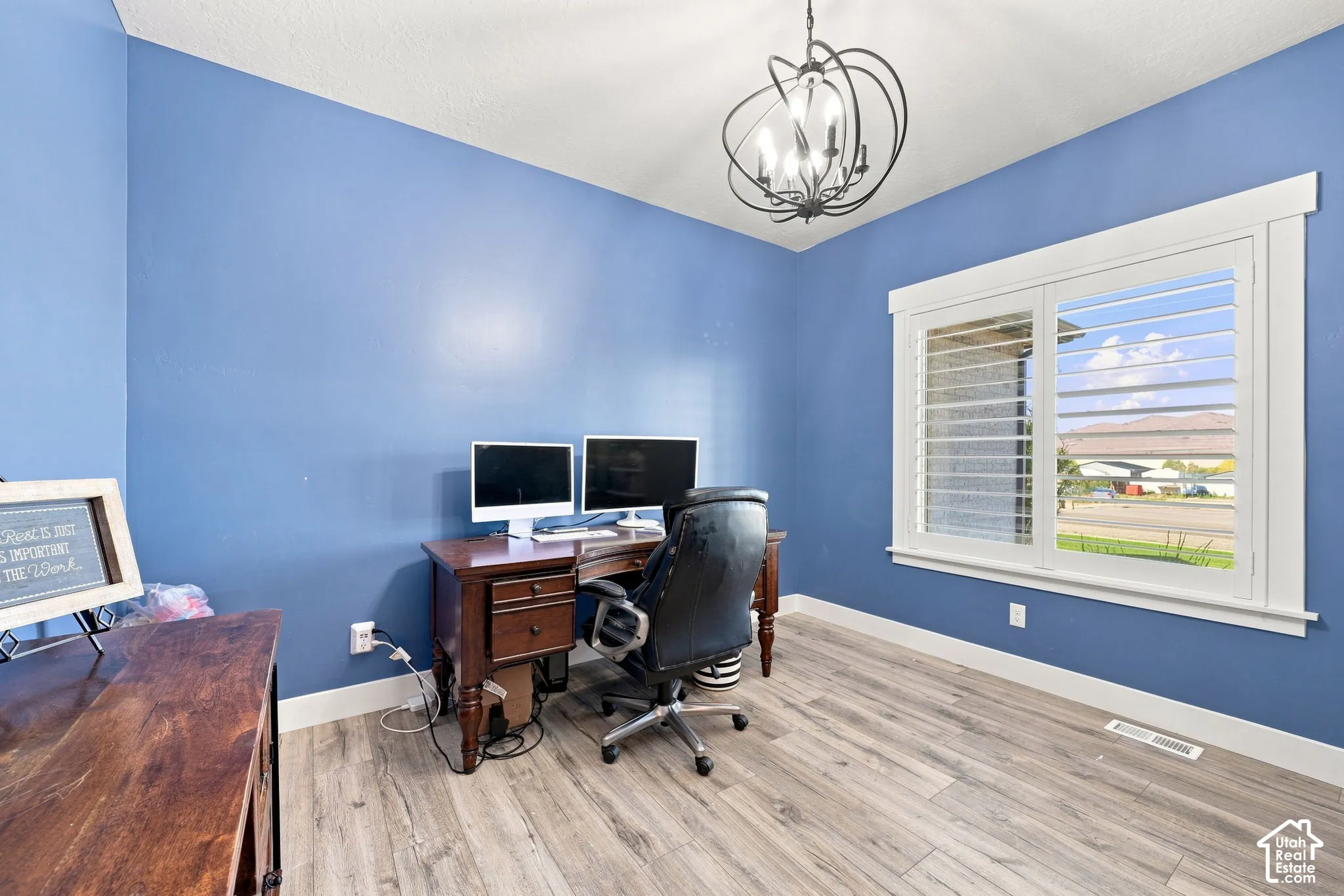 Room featuring wood-finish flooring, plantation shutters, and a multi-light spherical chandelier
