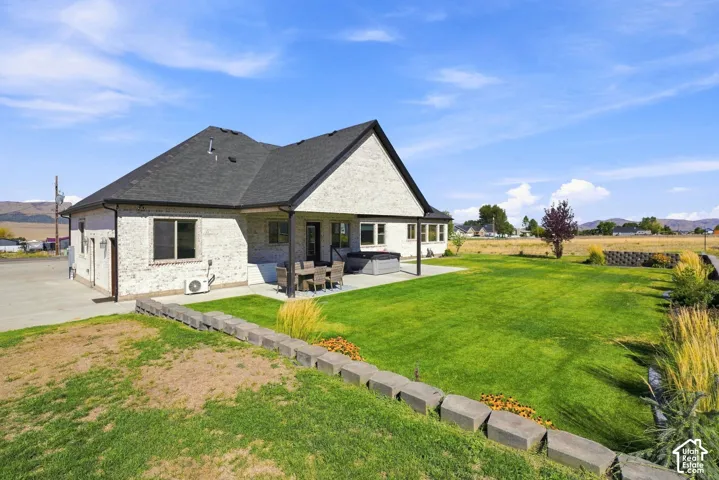 Brick exterior residence featuring a covered rear patio, expansive lawn, stone block retaining wall, and mountain backdrop