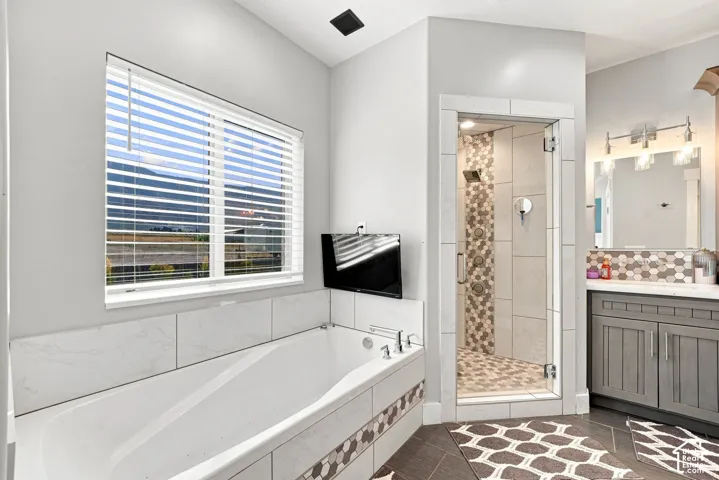 Deep soaking bathtub with stone-finish tile surround, glass-enclosed shower with mosaic stone tile detailing, and vanity with stone countertop