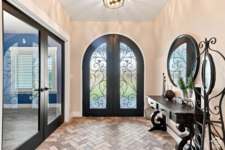 Arched double doors featuring black frames and intricate iron scrollwork, herringbone-patterned tile flooring, and glass-paneled double doors with black frames