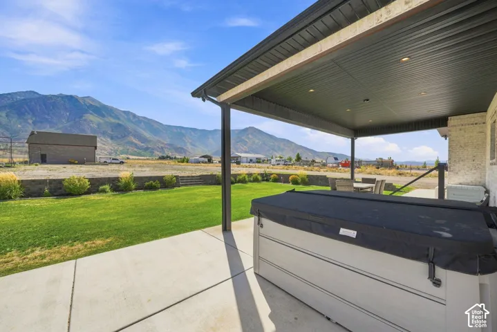 Covered concrete patio featuring recessed lighting, a built-in spa, a landscaped lawn, and mountain scenery