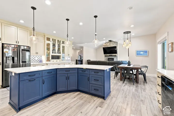 Kitchen featuring custom blue cabinetry, light-toned stone countertops, a large central island, recessed lighting, and wood-finish flooring