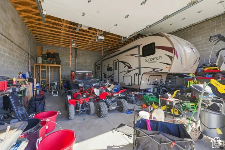 Oversized garage featuring exposed wood truss ceilings, concrete masonry unit walls, and concrete flooring