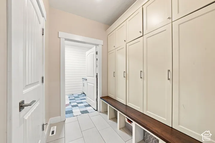 Floor-to-ceiling built-in cabinetry featuring shaker-style doors, a dark wood-finish bench seat, lower cubbies, and light-tone tile flooring