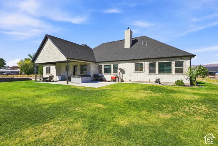 Brick exterior featuring a covered patio, concrete hardscaping, a shingled roof, and an expansive lawn