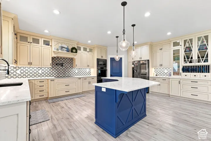 Kitchen featuring custom light-toned cabinetry with glass-front uppers, a central island with decorative woodwork, quartz countertops, patterned tile backsplash, and wood-finish flooring