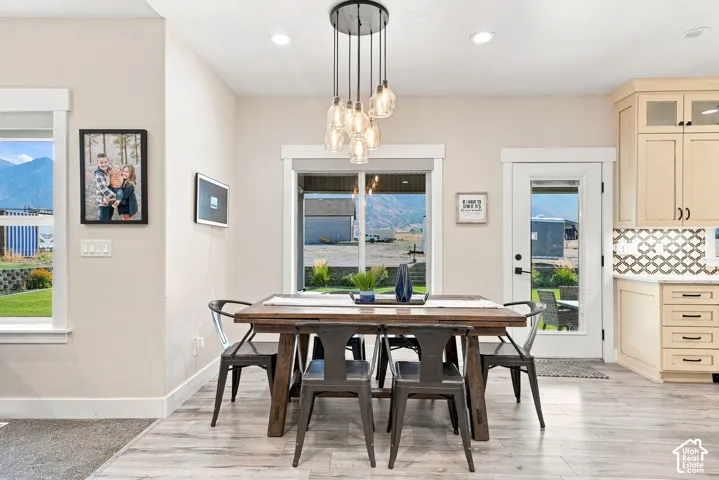 Multi-light glass pendant fixture, neutral cabinetry with upper glass-front accents, patterned tile backsplash, wood-finish flooring, and exterior door with glass insert