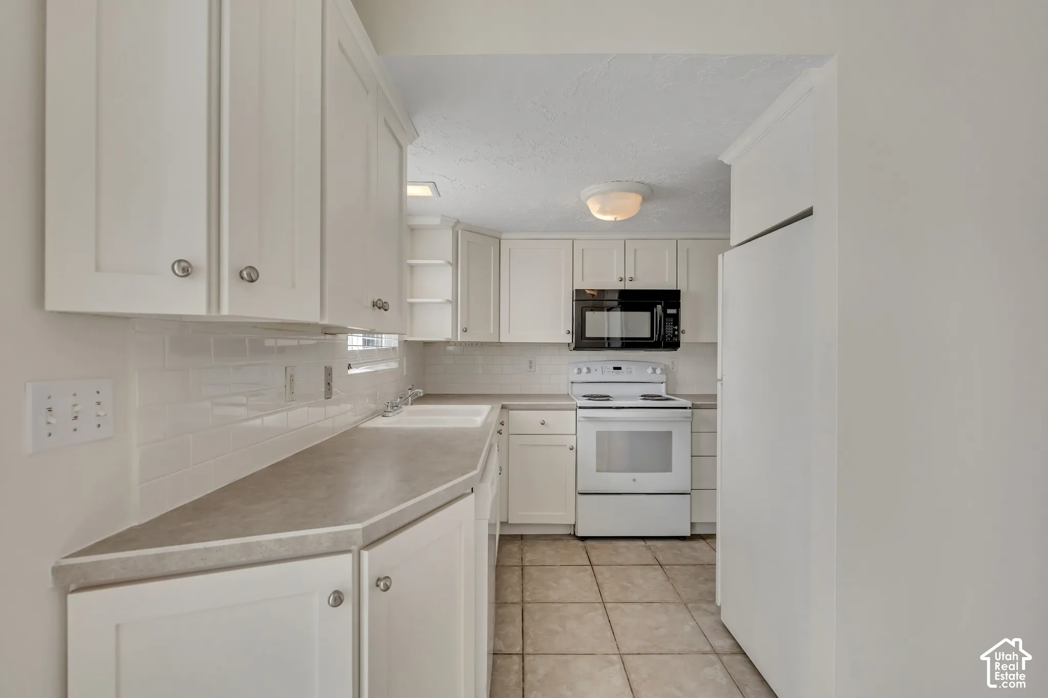 White cabinetry, solid surface countertops, white subway tile backsplash, and tile flooring