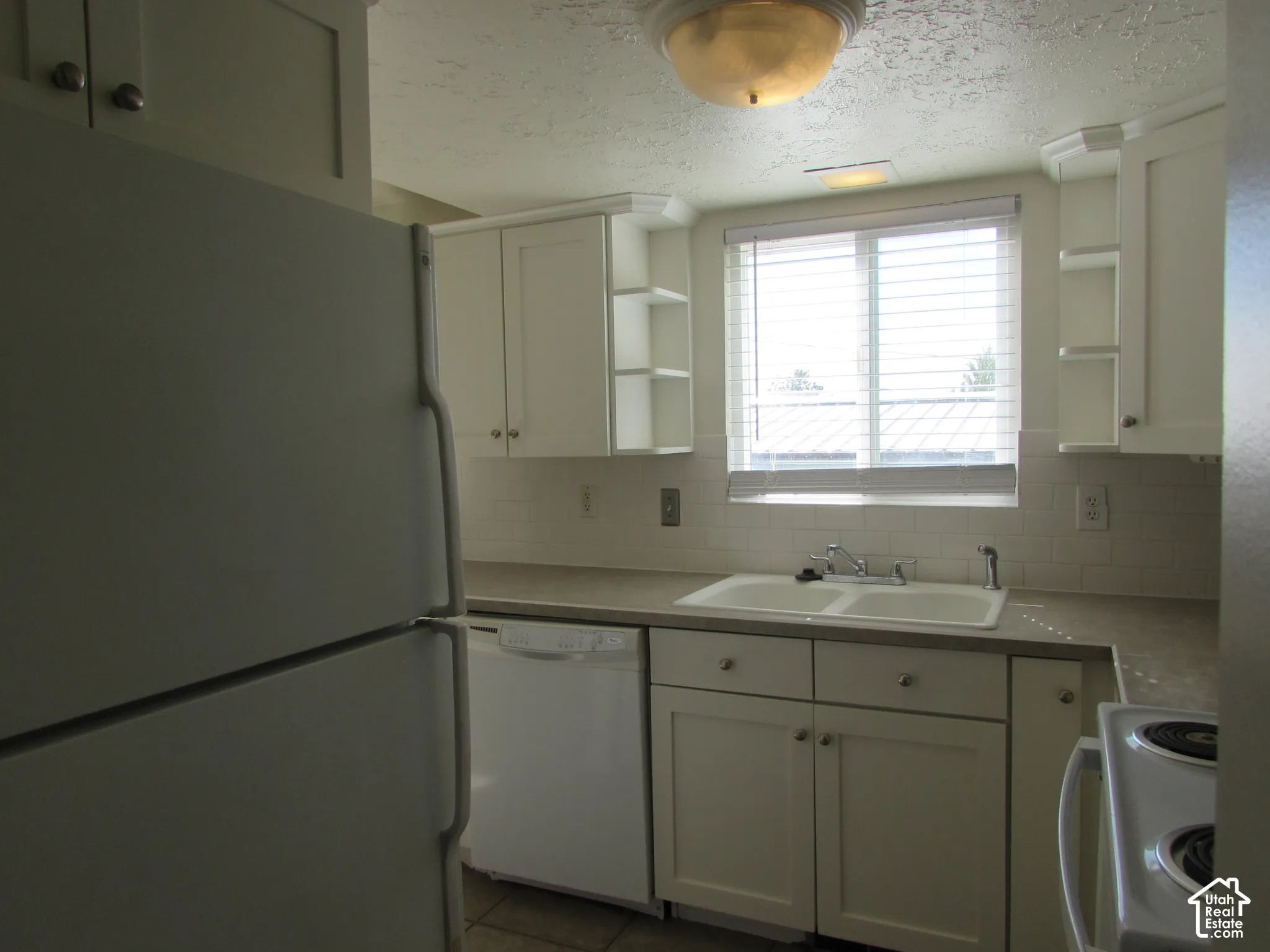 White kitchen cabinetry, dual basin sink, white subway tile backsplash, white built-in dishwasher, and a white refrigerator