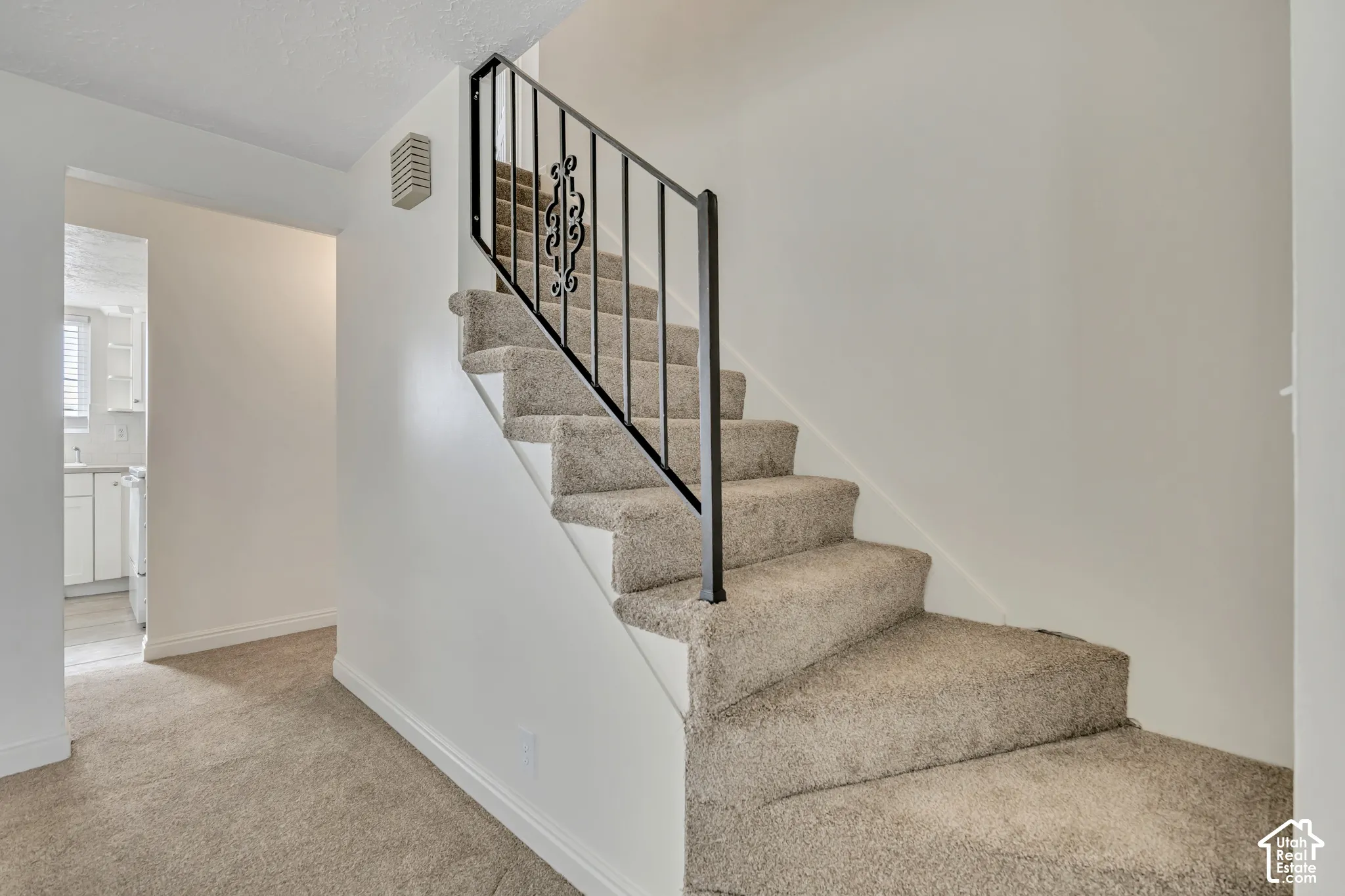 Carpeted staircase with black wrought iron railing and white walls