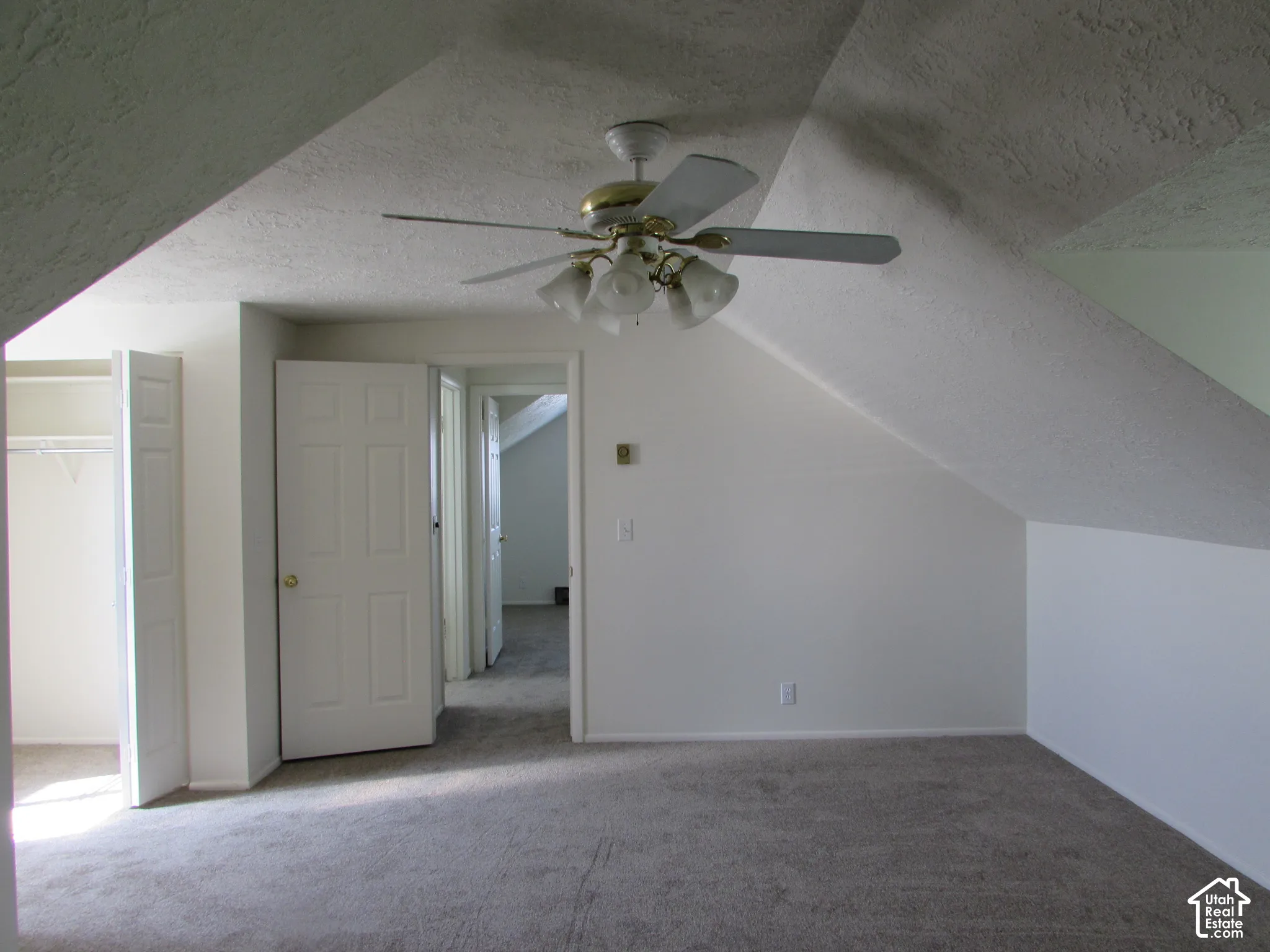 Sloped ceiling, ceiling fan with light fixture, wall-to-wall carpeting, white paneled doors, and an open closet with wire shelving