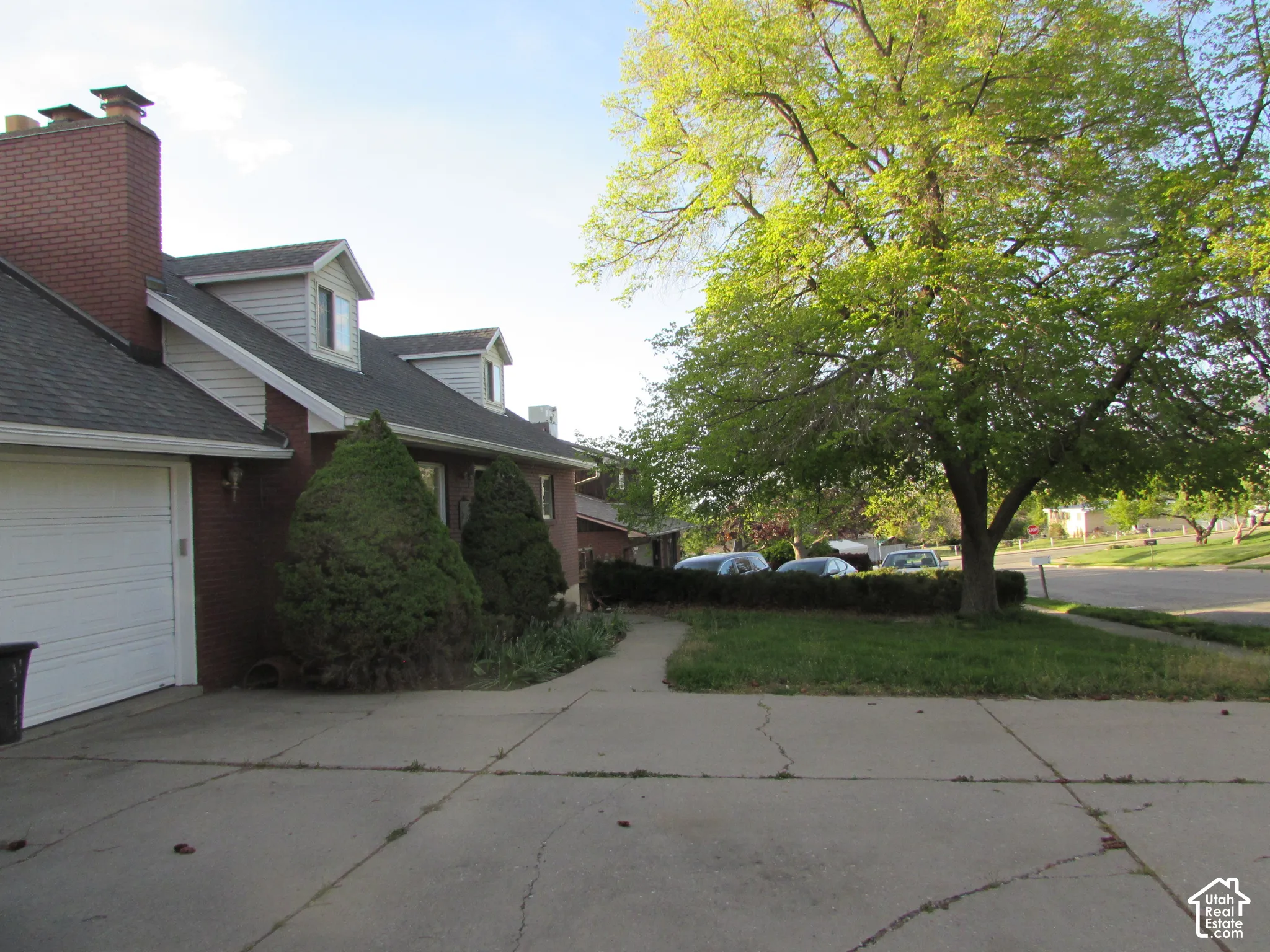 Brick exterior with dormer windows, attached garage, and a mature shade tree