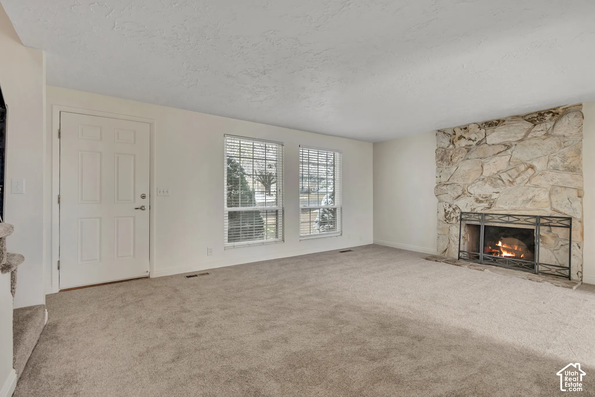 Carpeted living space featuring a natural stone fireplace and two windows