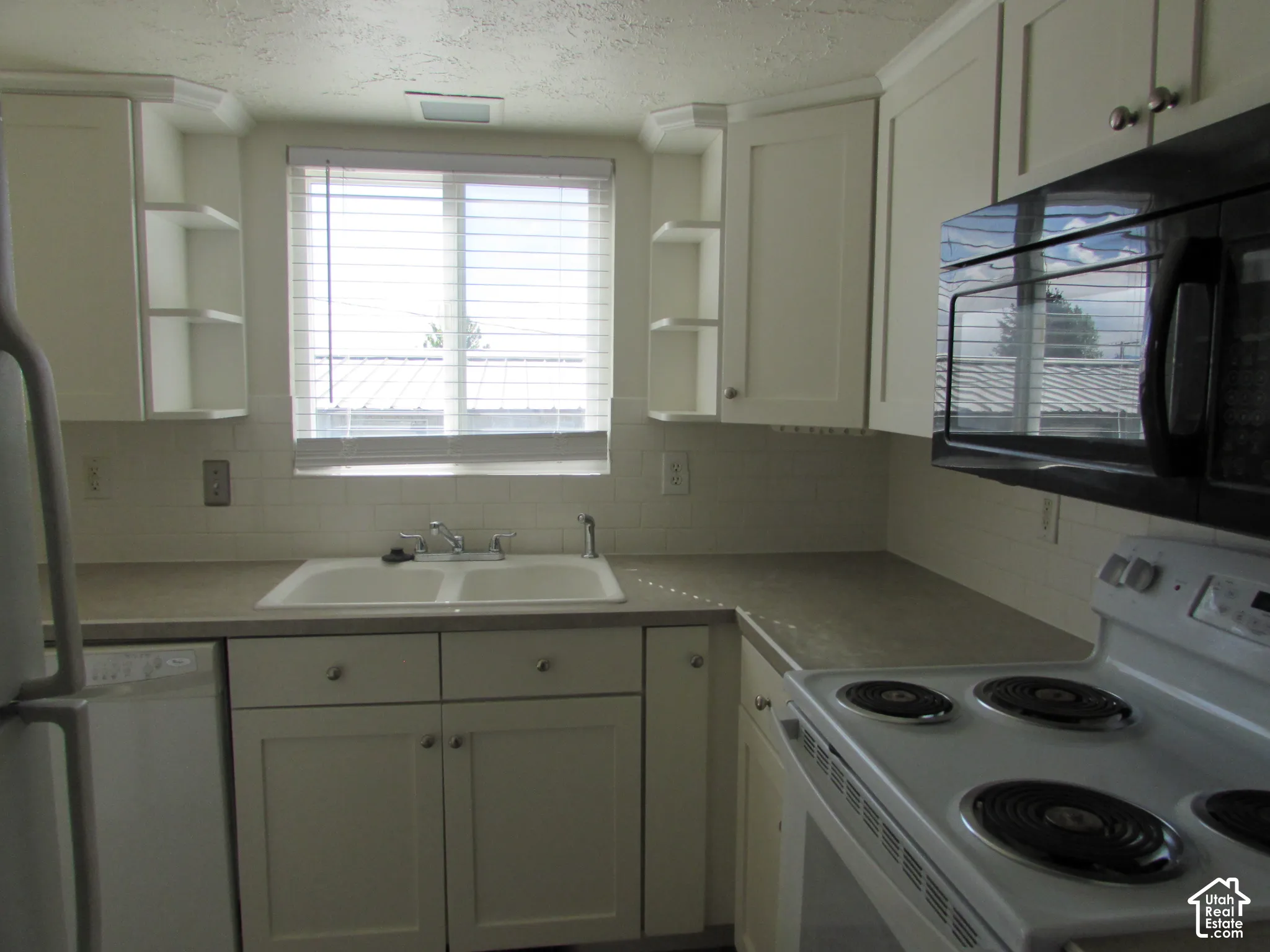 White cabinetry with brushed nickel hardware, white subway tile backsplash, laminate countertops, and a double basin sink