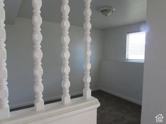 White painted balusters with a dark carpeted floor, white walls, and a window with horizontal blinds