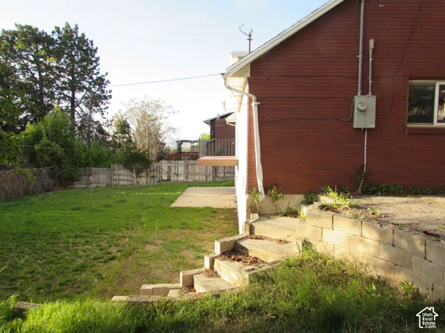 Expansive grassy yard with a concrete patio, wood fence, and mature trees