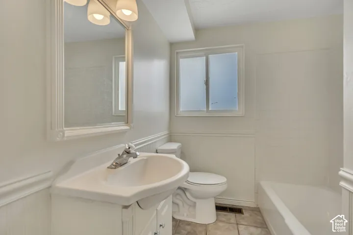 White vanity with an integrated sink and chrome faucet, framed mirror with sconce lighting, beadboard wainscoting, and a window with frosted panes