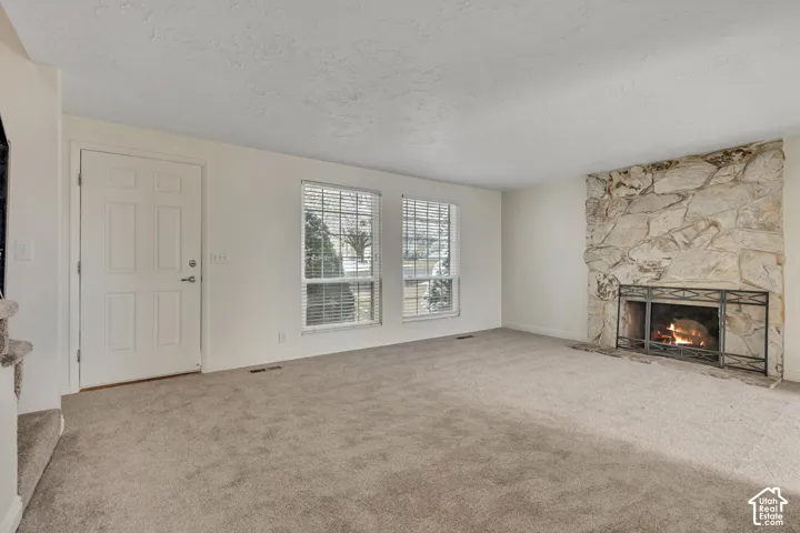 Carpeted living space featuring a natural stone fireplace and two windows
