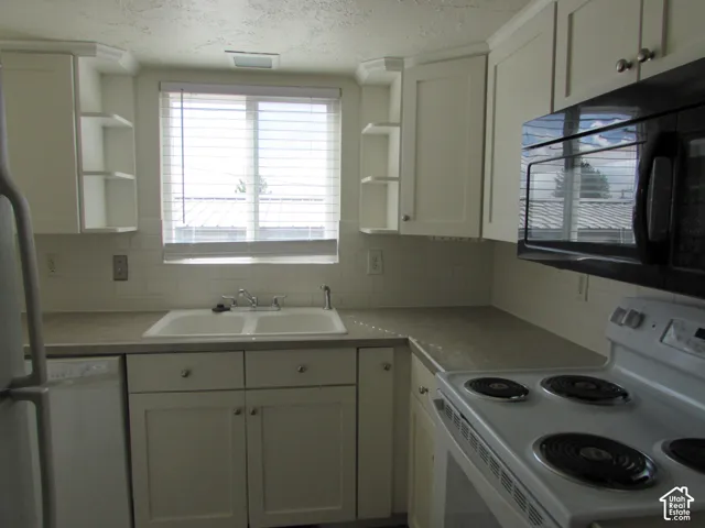 White cabinetry with brushed nickel hardware, white subway tile backsplash, laminate countertops, and a double basin sink