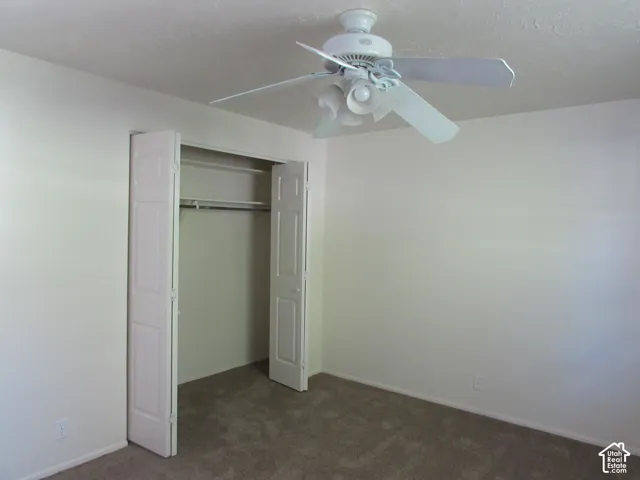 Neutral wall paint, carpeted flooring, bi-fold closet doors, integrated closet shelving, and a ceiling fan with light fixture