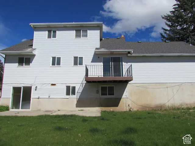 White siding exterior with multiple windows, second-story balcony with metal railing, and ground-level sliding glass door
