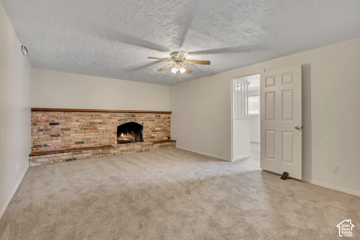 Brick fireplace with wood mantel, ceiling fan, and carpeted flooring