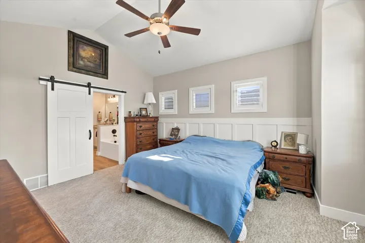 Vaulted ceilings, white wainscoting, sliding barn door with black hardware, and three windows with shutters