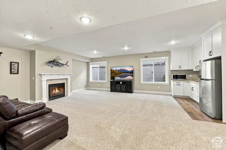 Open-concept interior featuring a fireplace with a white mantel, recessed lighting, white cabinetry with integrated stainless steel appliances, and a combination of carpeted and wood-finish flooring